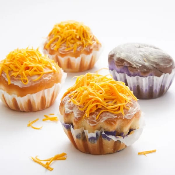 Four Goldilocks ensaymadas, three topped with bright orange cheese, one with purple ube frosting.
